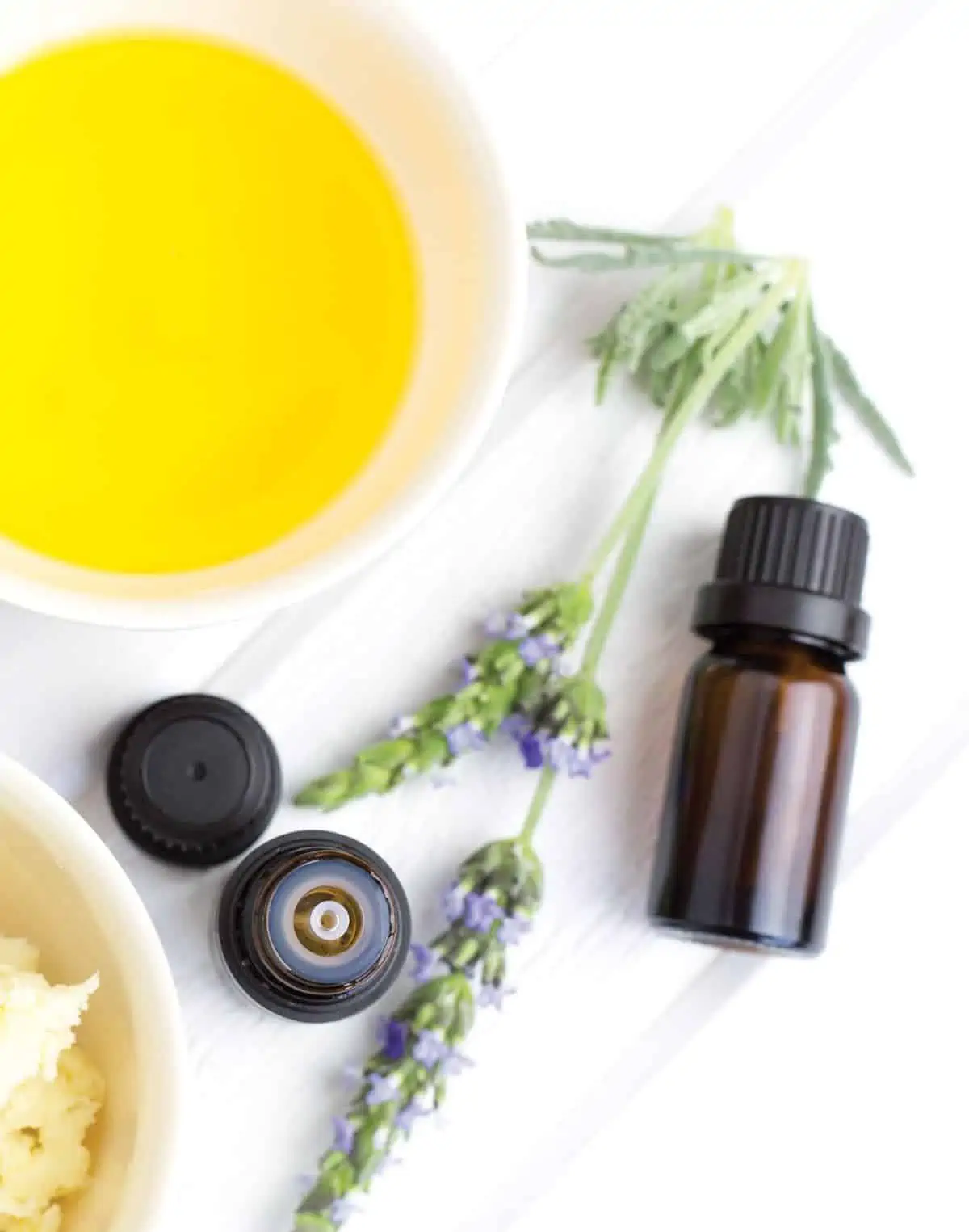 Essential oil perfume in glass bottle next to bowl of melted wax.