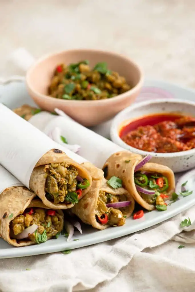 vegan chana kathi rolls wrapped in paper with a red chutney on the side. the rolls are roti bread filled with spiced chickpeas