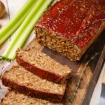 Vegan meatloaf on a cutting board with a few slices cut off laying next to it.