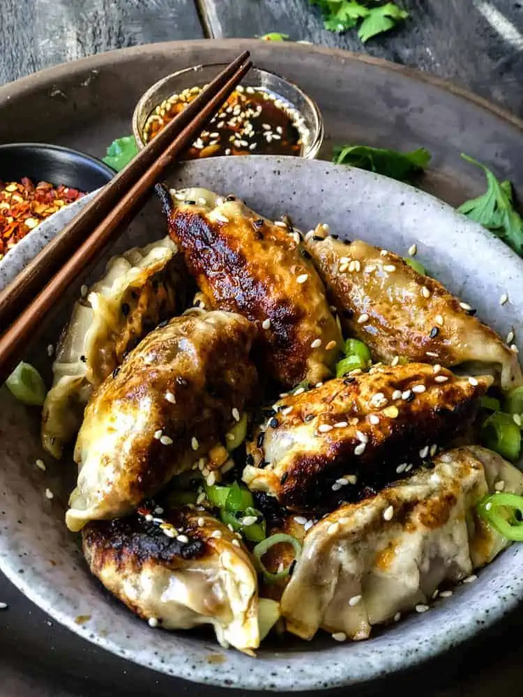 vegan potstickers garnished with sesame seeds and scallions in a bowl with chopsticks