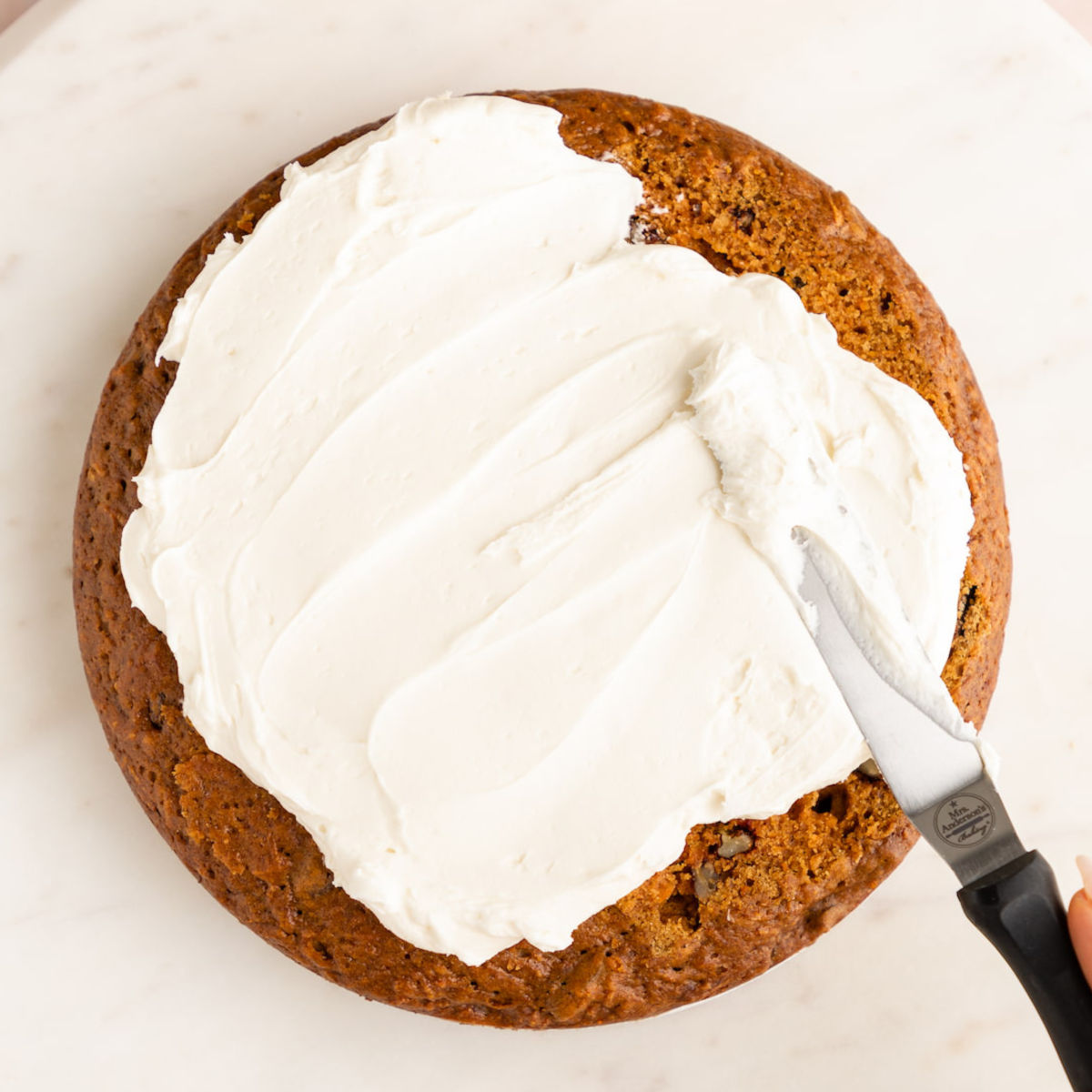 Dairy-free cream cheese frosting being spread over the top of a vegan carrot cake.