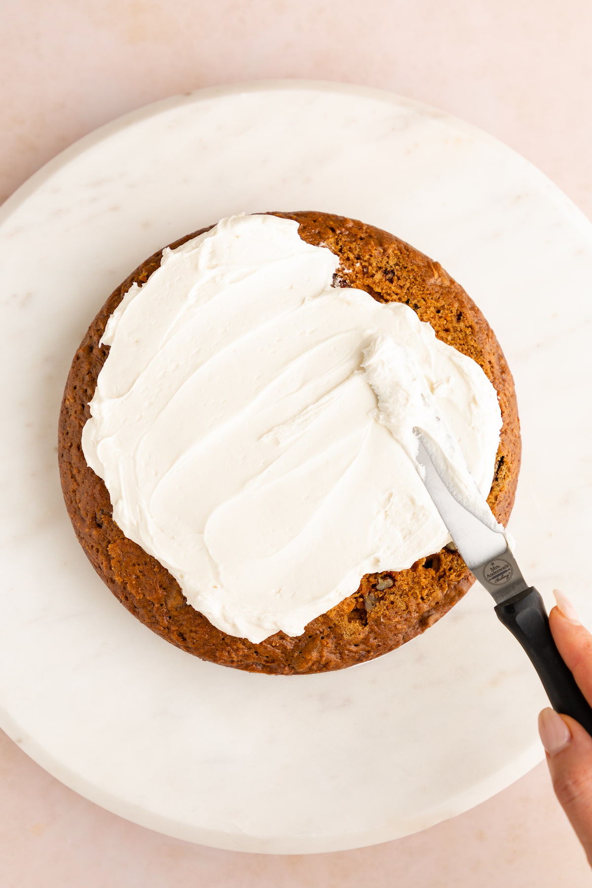 Spreading thick vegan cream cheese frosting on a homemade carrot cake.