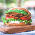 Slices of tofu bacon piled on a sandwich with lettuce and tomato slices.