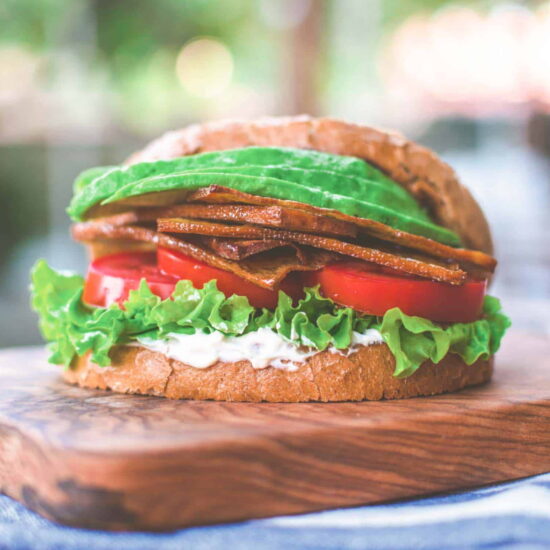 Slices of tofu bacon piled on a sandwich with lettuce and tomato slices.