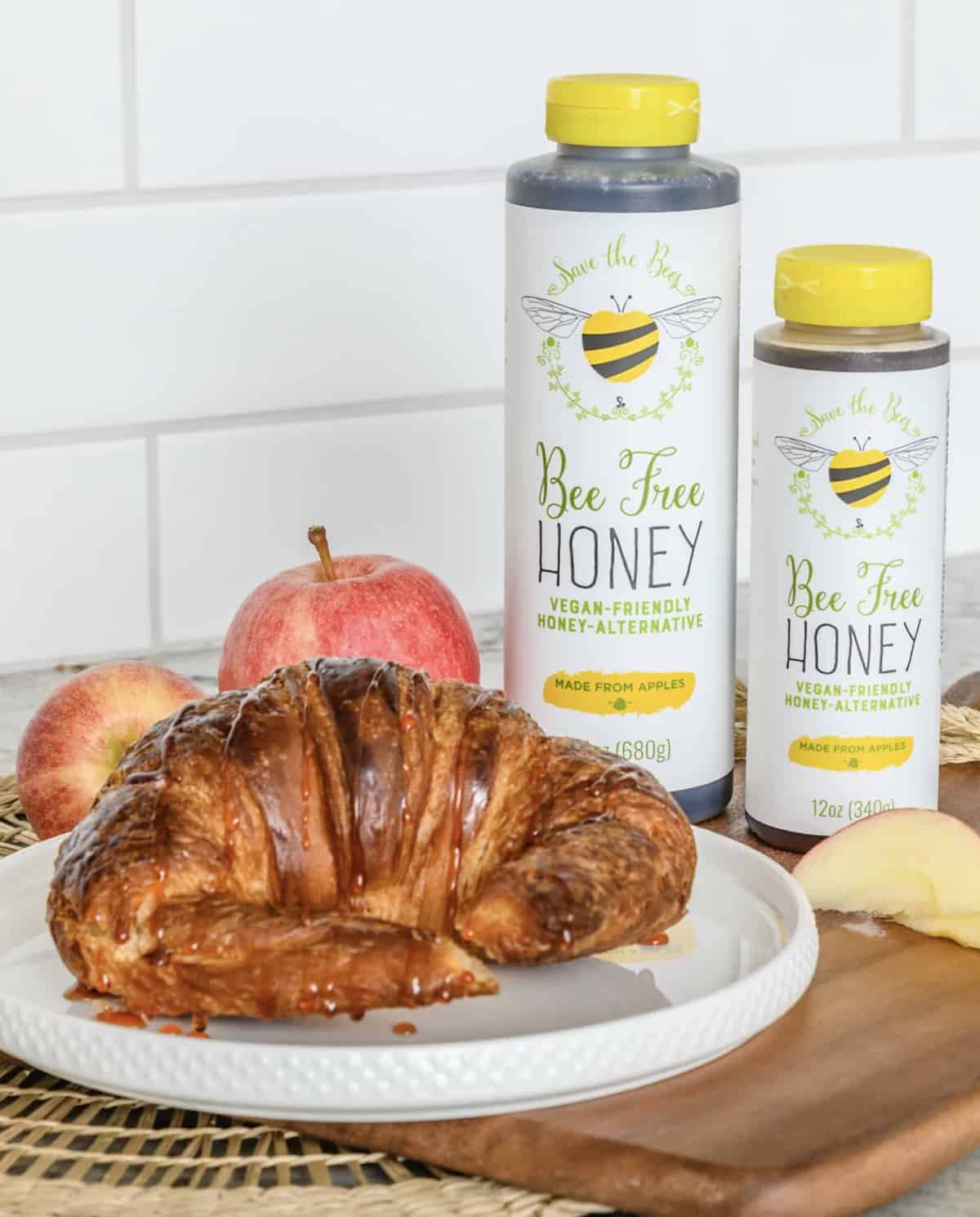 Store-bought bottles of organic vegan bee-free honey made from apples next to a croissant.