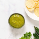 A bowl of tomatillo salsa next to a bowl of tortilla chips.