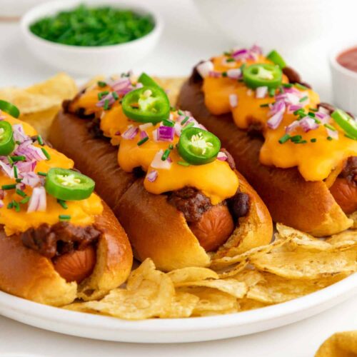 Three vegan chili cheese dogs with plant based cheese served on a plate.