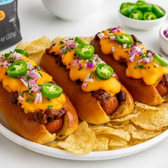 three vegan chili cheese dogs on a plate surrounded by toppings