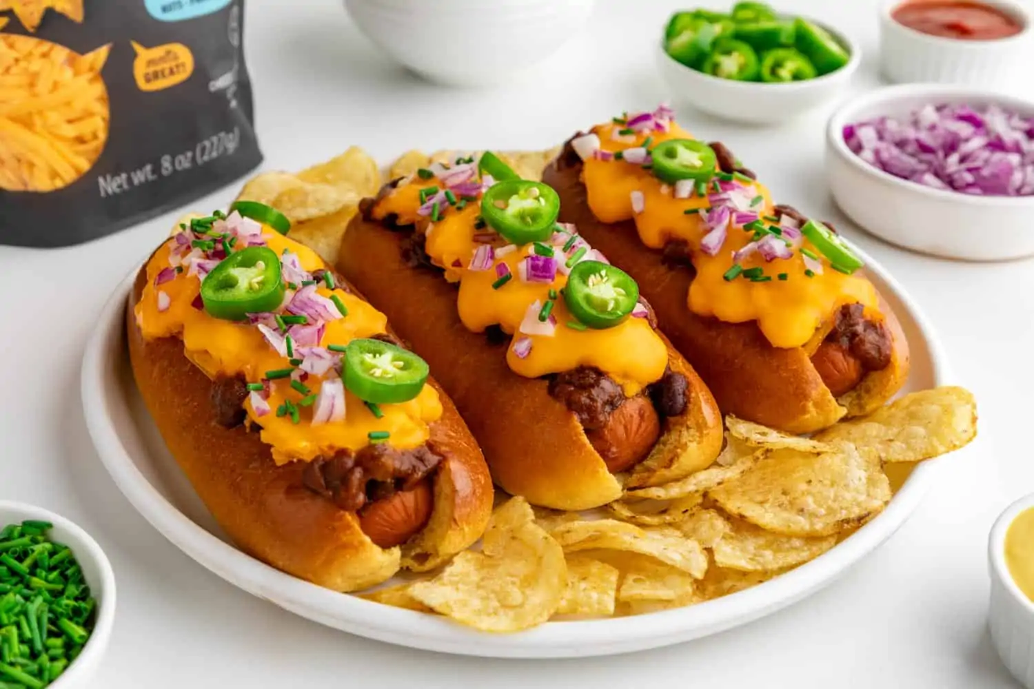 three vegan chili cheese dogs on a plate surrounded by toppings