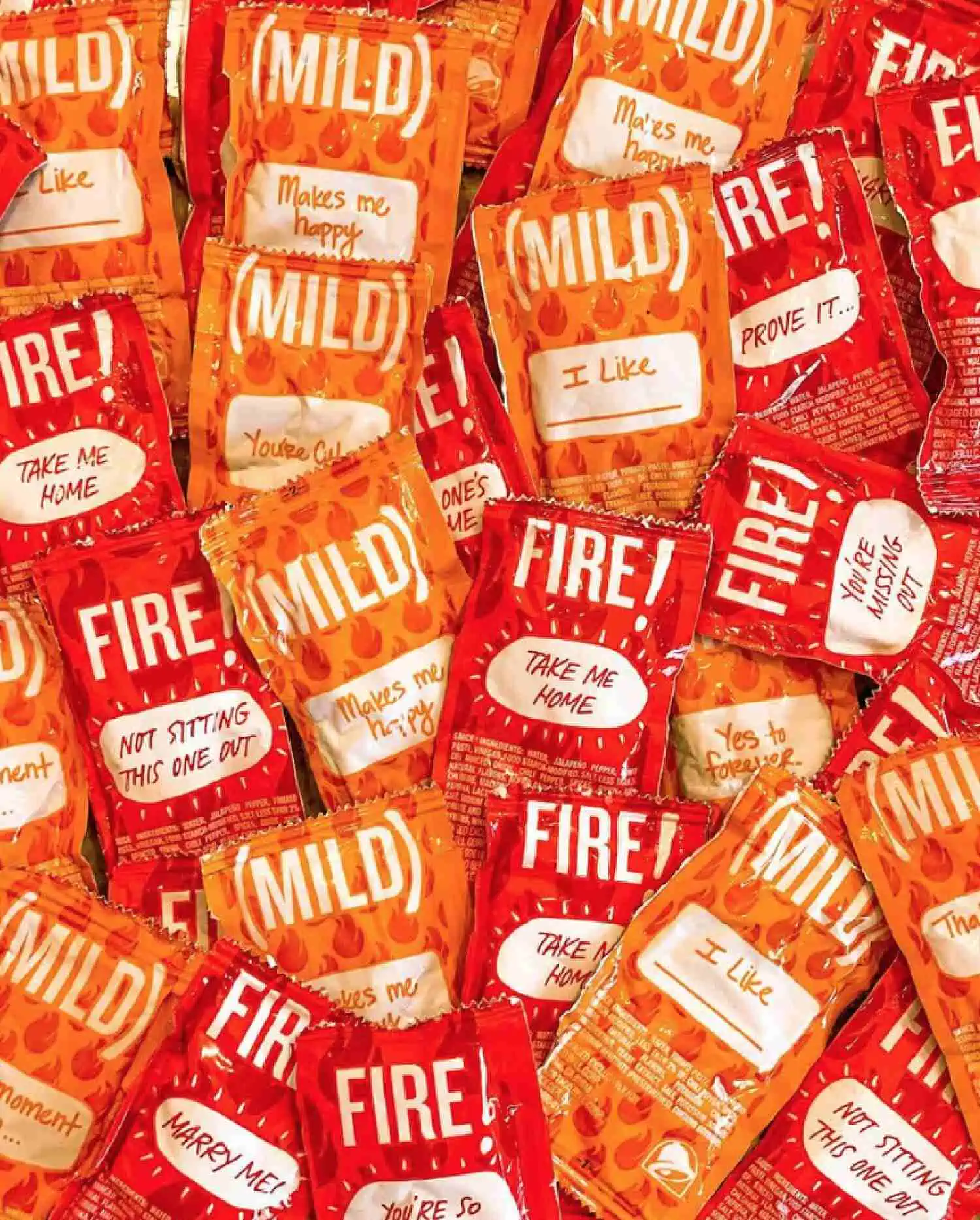 A pile of red and orange colored hot sauce packets with the spiciness level and a saying written on each one.