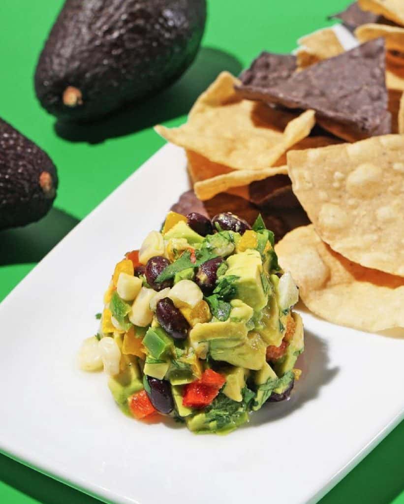 White plate with a large scoop of white corn guacamole and tortilla chips on the side. 