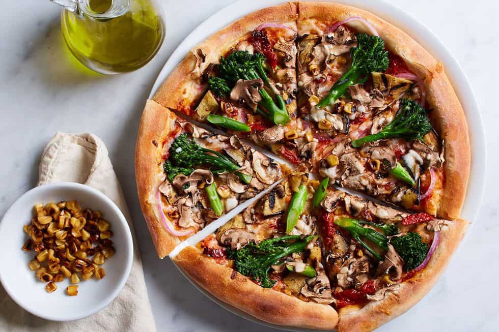 A full California Veggie Pizza from CPK topped with broccoli and served with red pepper flakes and olive oil. 