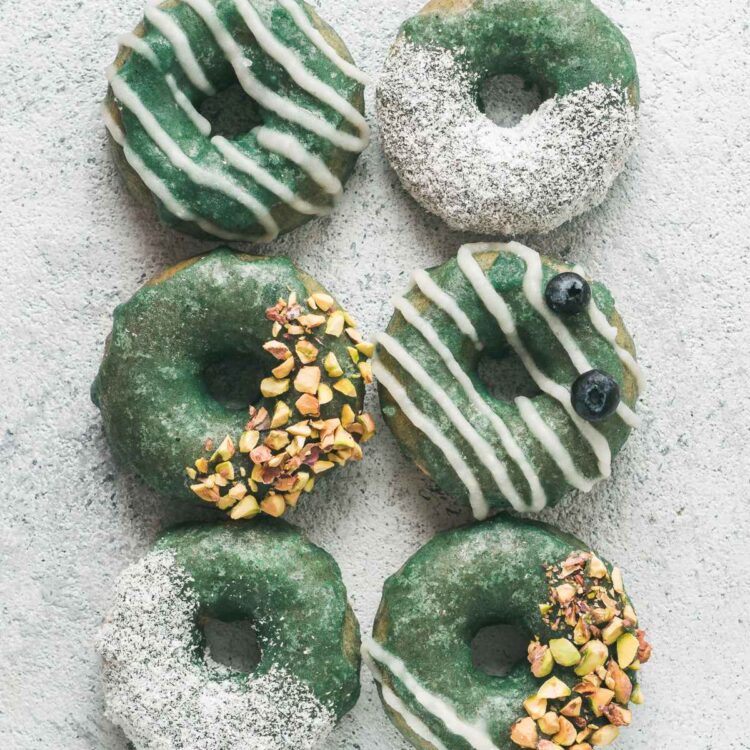 Six vegan donuts with green and white frosting and chopped nuts on top.