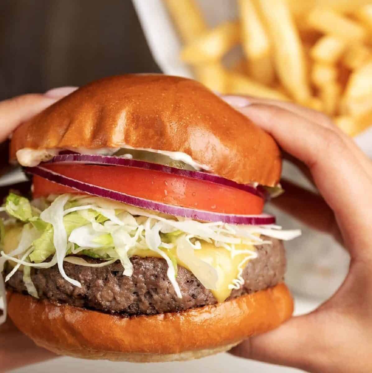 Hands holding up an Impossible Glamburger from the Cheesecake Factory.