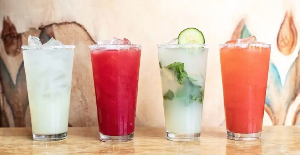 Four glasses of flavored lemonade lined up next to each other on a countertop.