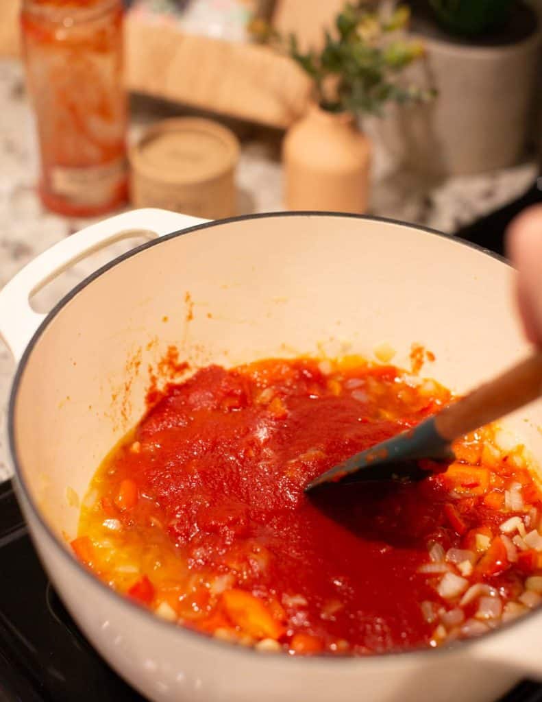 adding tomato sauce to sauteed onions in a cast iron dutch oven