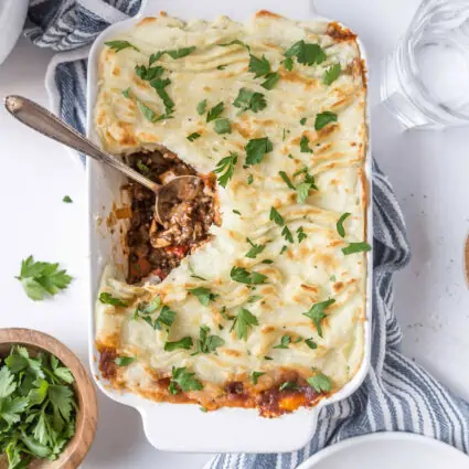 Vegan Shepherd's Pie in a casserole dish with a serving spoon and a serving missing.