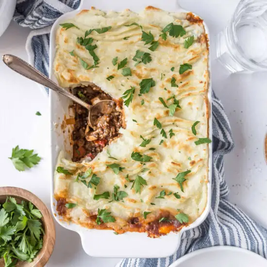 Vegan Shepherd's Pie in a casserole dish with a serving spoon and a serving missing.