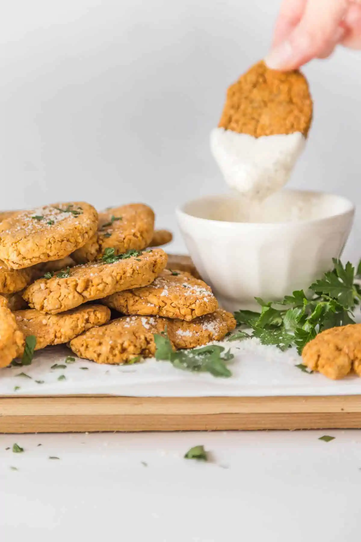 Pile of chickpea nuggets next to a bowl of vegan ranch dip with a dipped nugget hovering over the bowl.