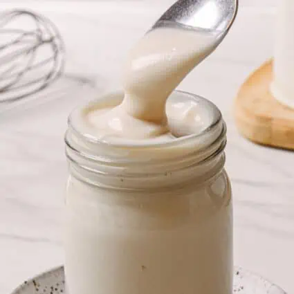 Mason jar with a spoon scooping out homemade vegan condensed milk.