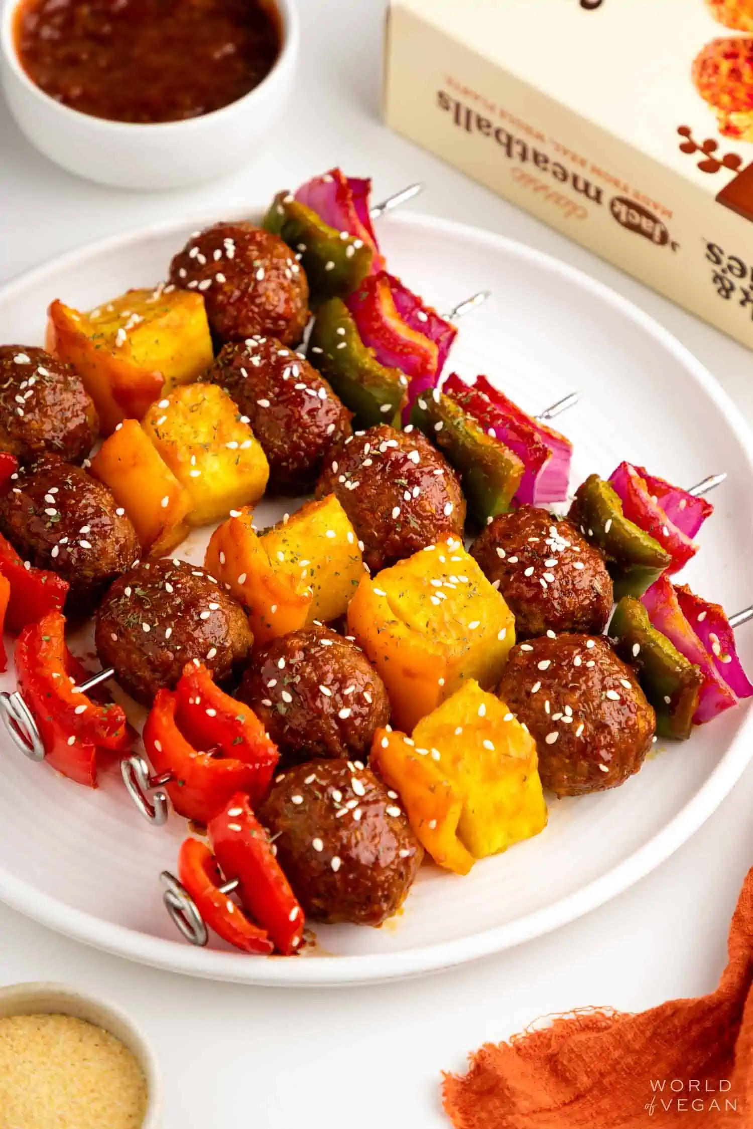 Vegan kabob skewers with veggies meatballs pineapple and sweet and sour sauce on a plate.