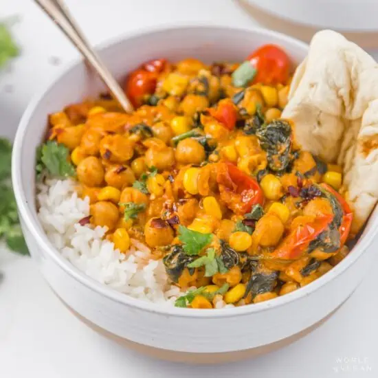 chickpea curry with spinach served in a bowl with rice and roti