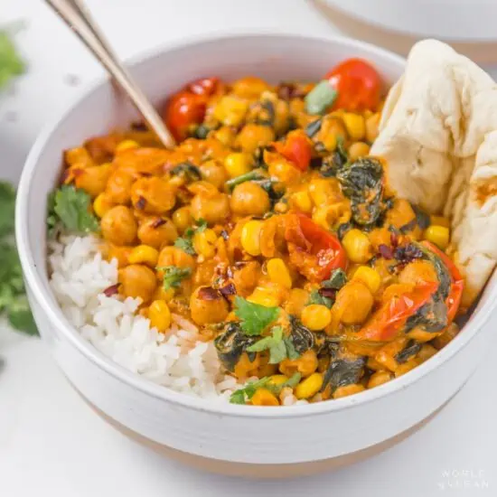 Chickpea curry with spinach served in a bowl with rice and roti.
