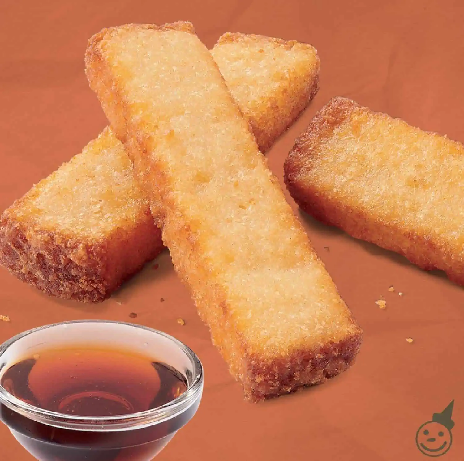 Three rectangular Jack in the Box French Toast Sticks on a brown background and sitting next to a small glass bowl of pancake syrup.