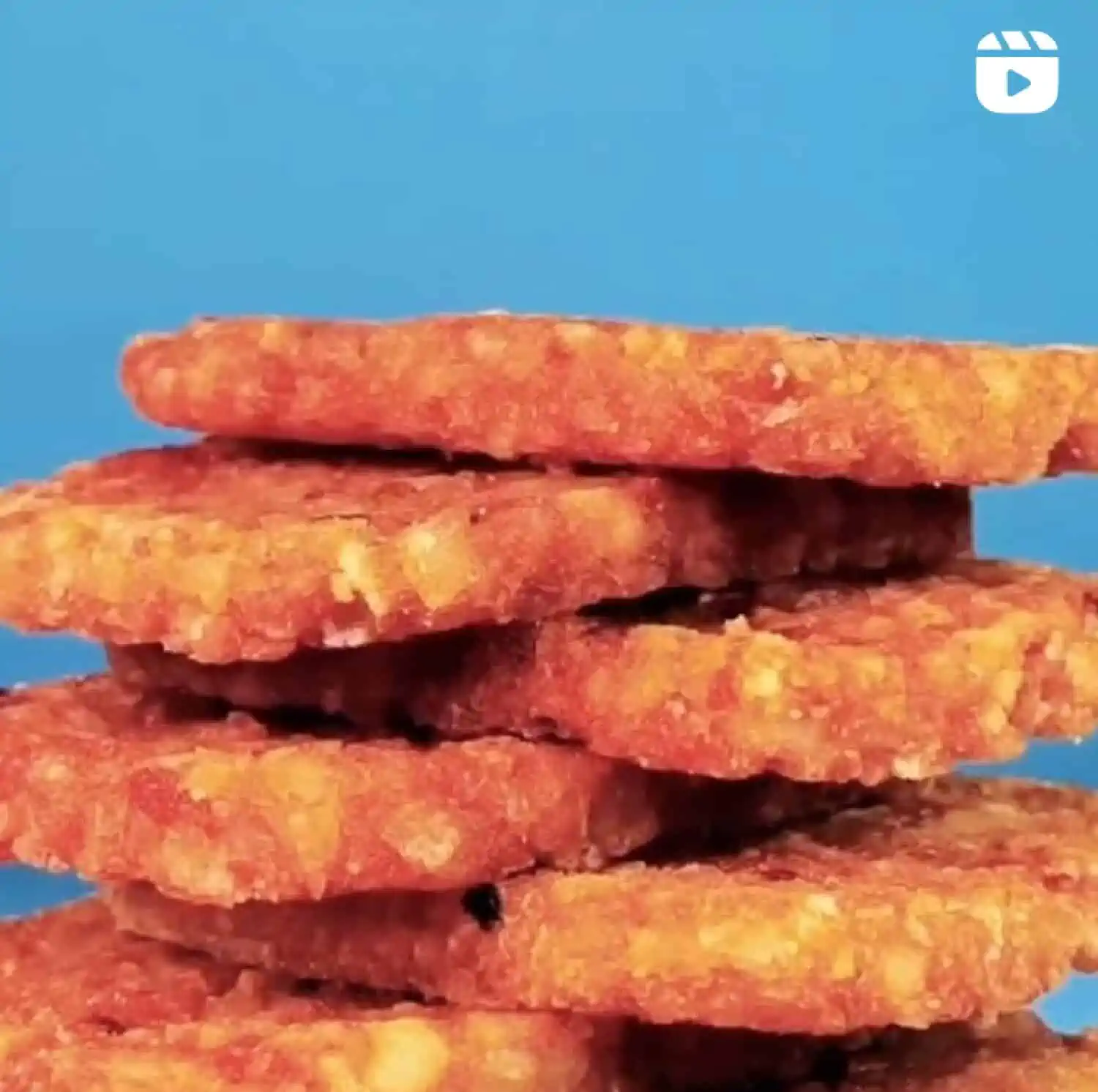 A vertical stack of six Jack in the Box hash brown patties alternately arranged at the bottom of the photo against a blue background. 