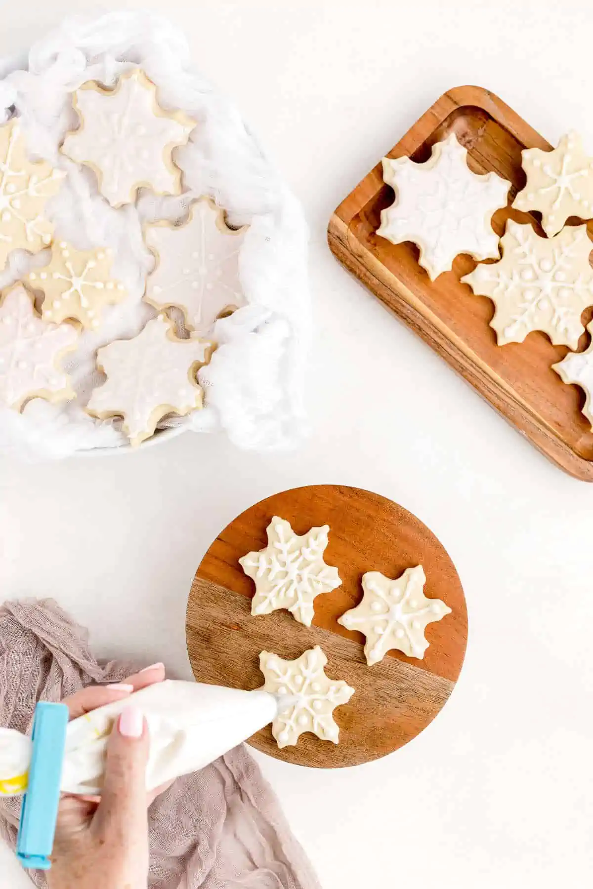 Hand piping vegan royal icing onto sugar cookies shaped like a snowflake.