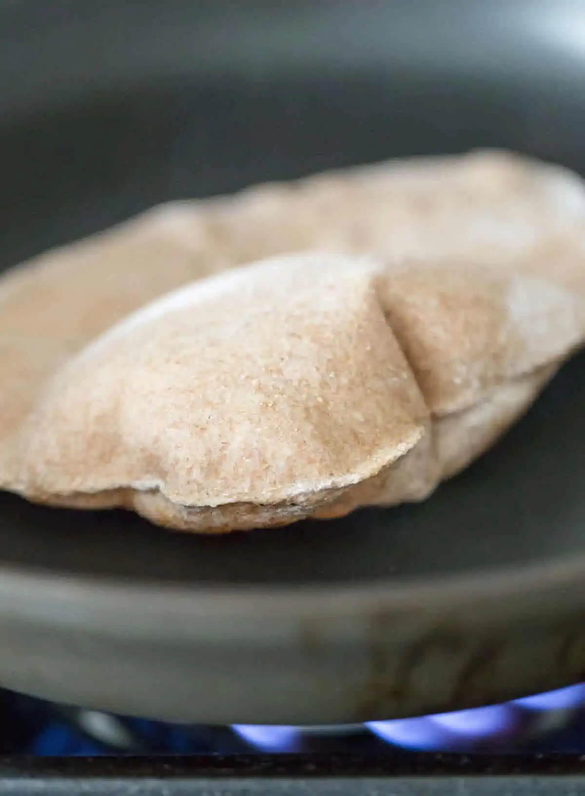 A piece of vegan roti puffed up in a pan while cooking.