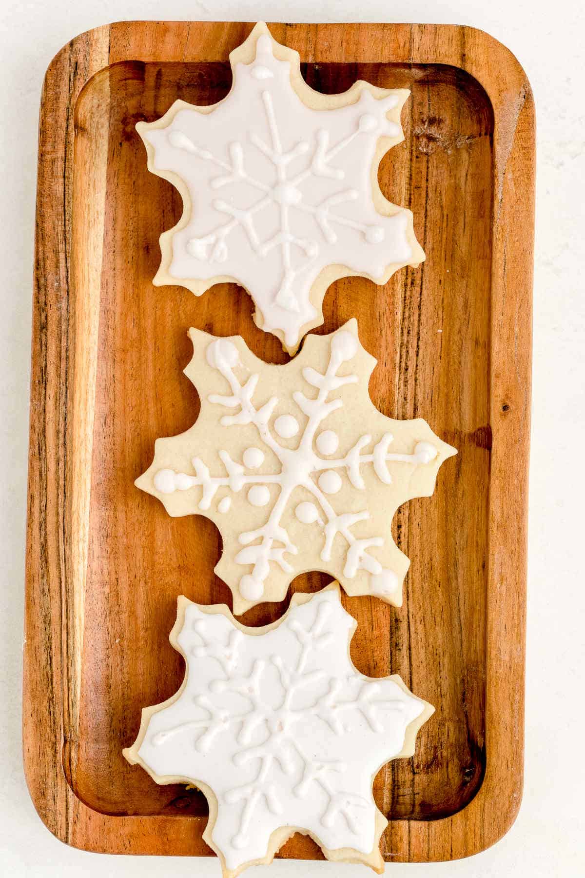 Snowflake-shaped sugar cookies on wooden plate decorated with eggless royal icing.