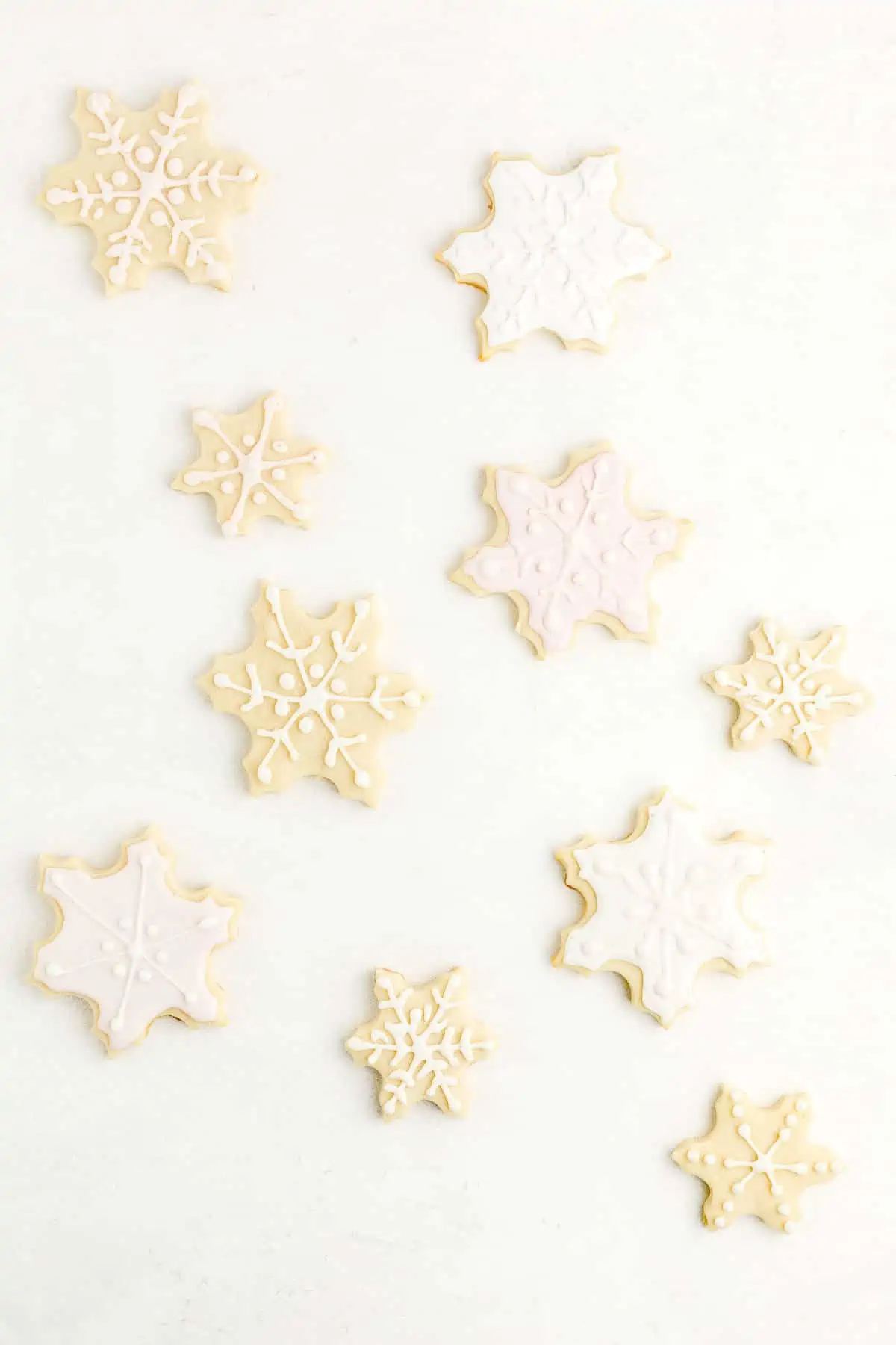 Snowflake-shaped sugar cookies on light background decorated with egg-free royal icing.