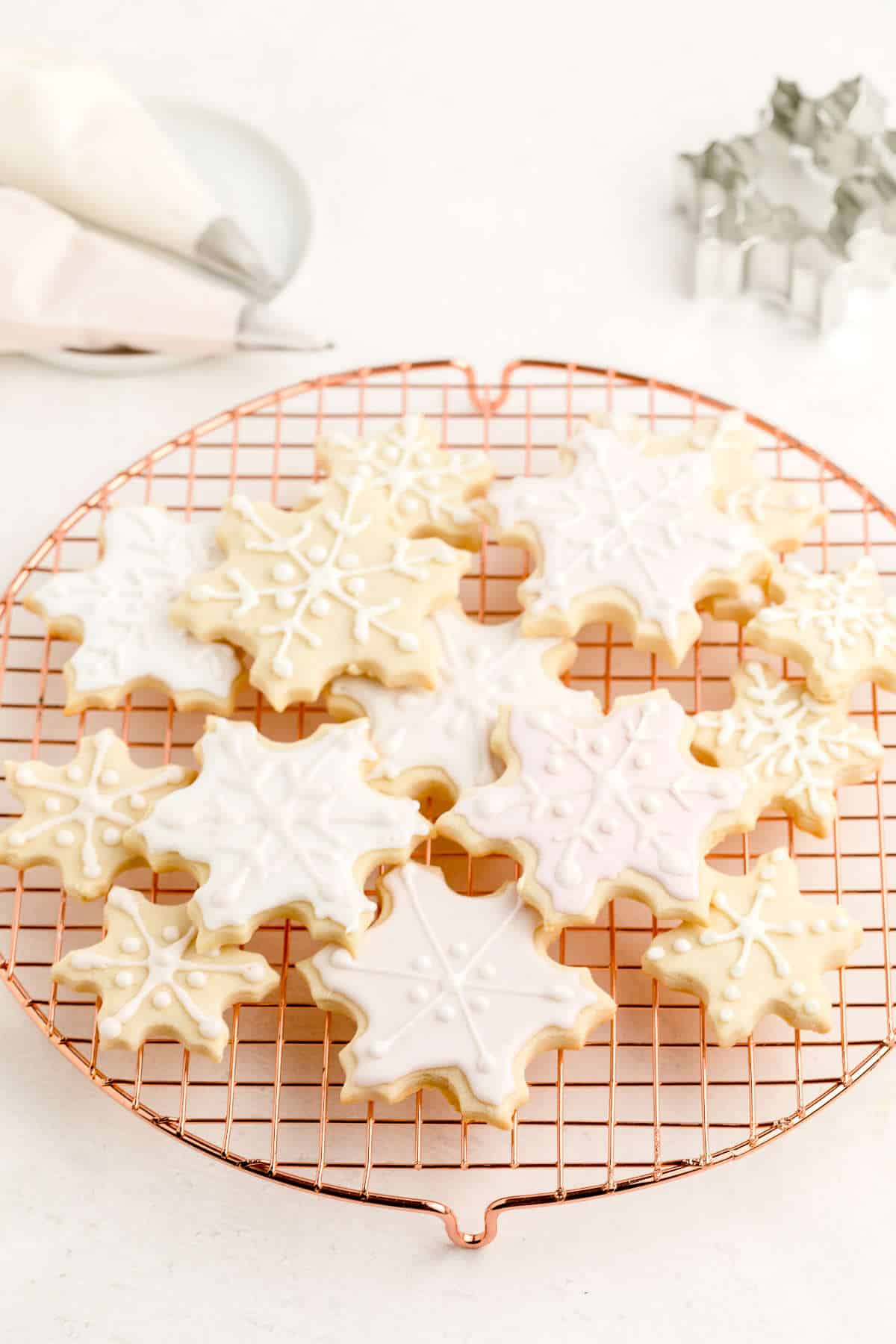 Snowflake-shaped sugar cookies decorated with vegan royal icing and sitting on a drying rack.