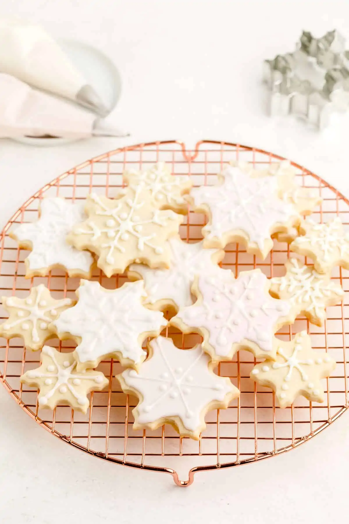 Snowflake-shaped sugar cookies decorated with vegan royal icing and sitting on a drying rack.