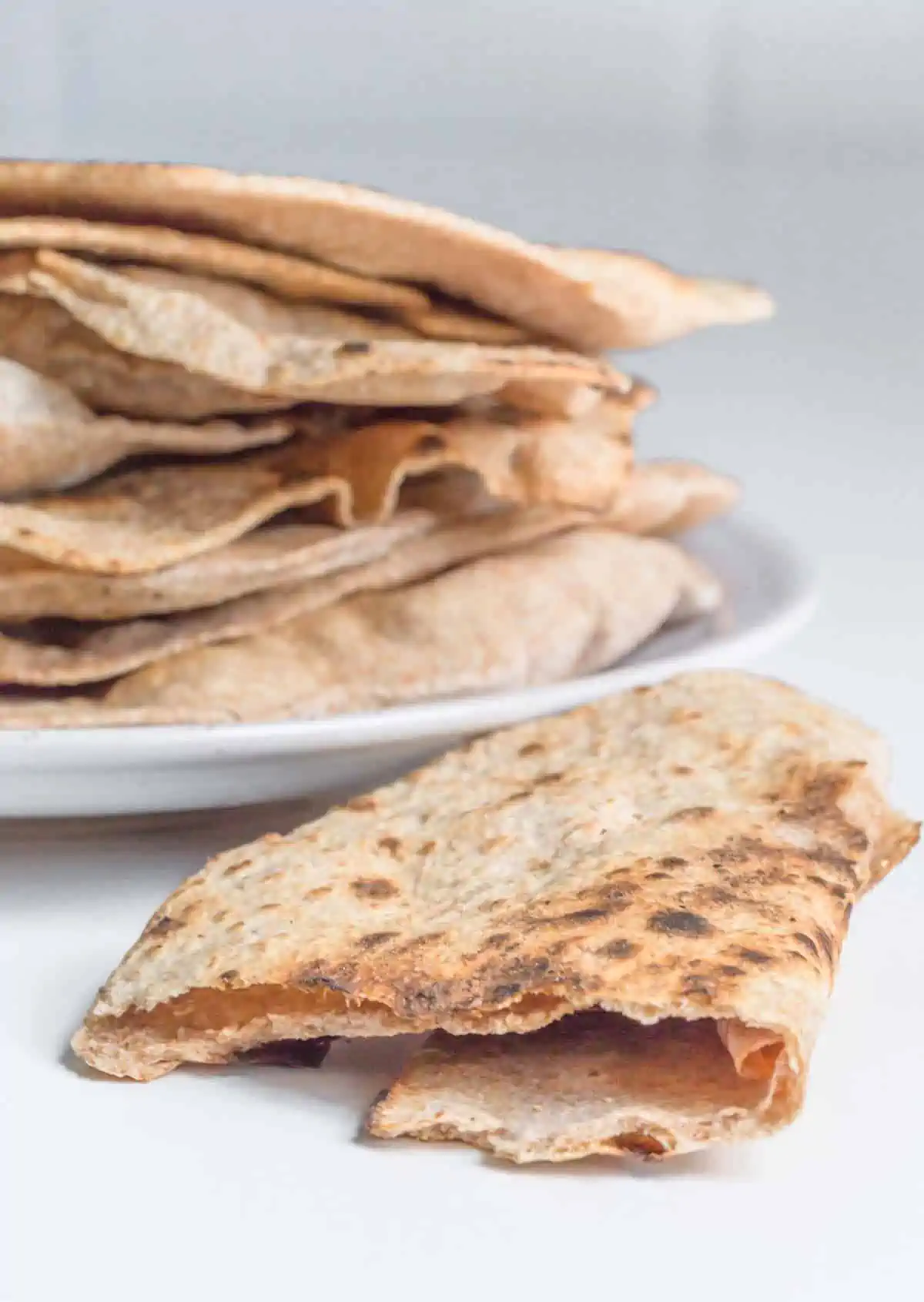 Vegan roti flatbreads stacked on a plate with one folded laying beside it.