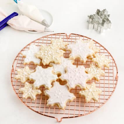 Snowflake-shaped sugar cookies decorated with vegan royal icing and sitting on a drying rack.