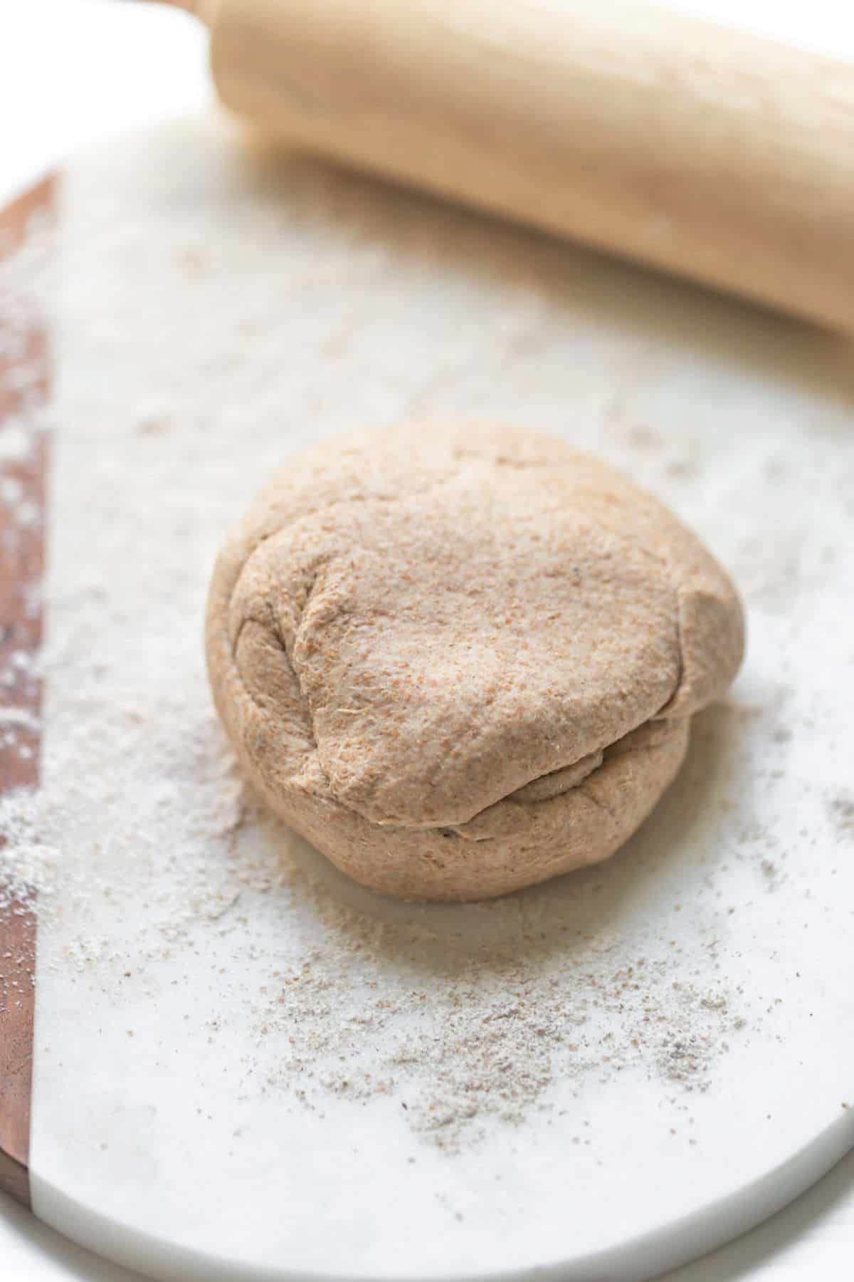 Roti dough rolled into a ball on a floured surface.