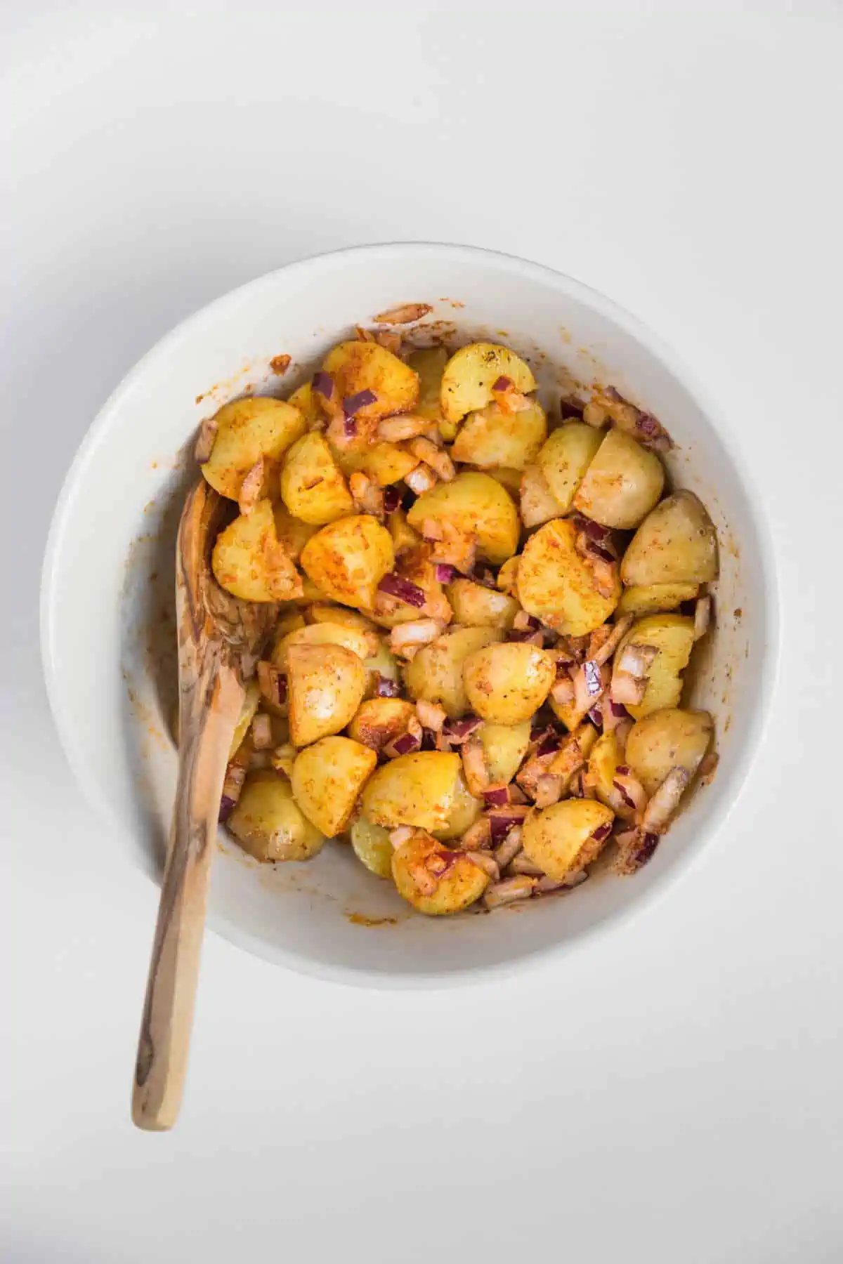 A large mixing bowl with potatoes, onions and seasonings all mixed together.