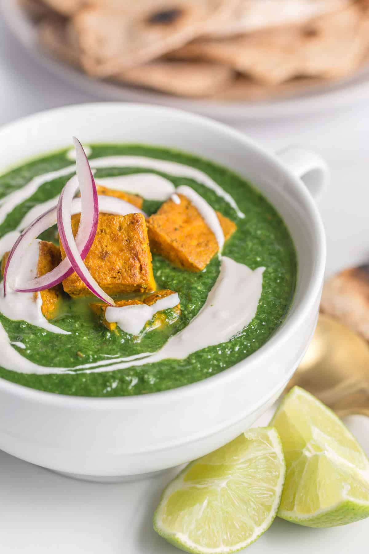 Palak tofu served in a bowl with roti and topped with red onions and vegan yogurt.