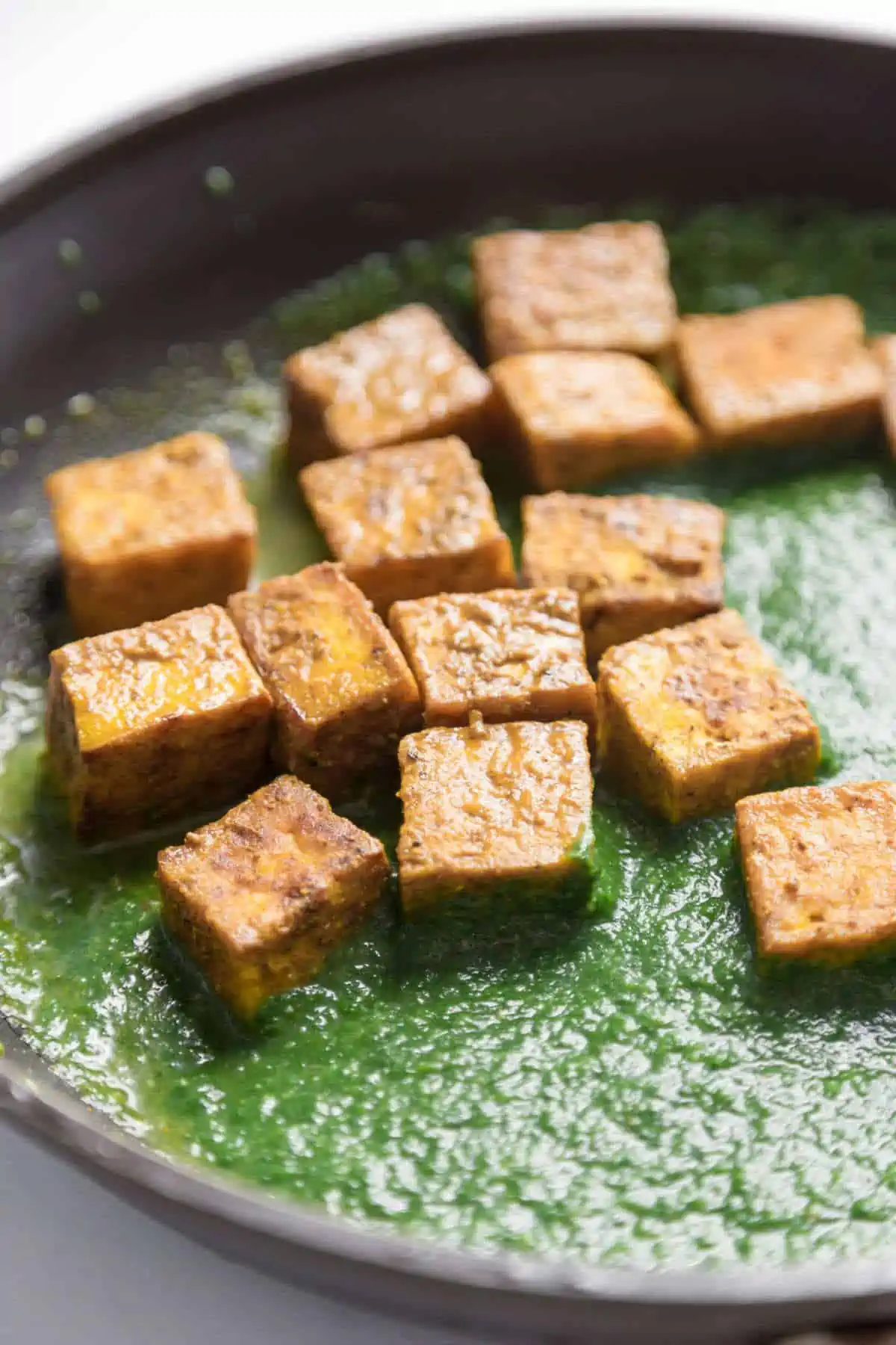 Palak tofu in spinach curry sauce in pan.