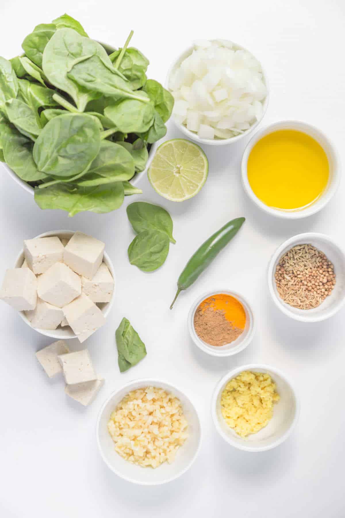 Ingredients for palak tofu measured in individually bowls on a light background.