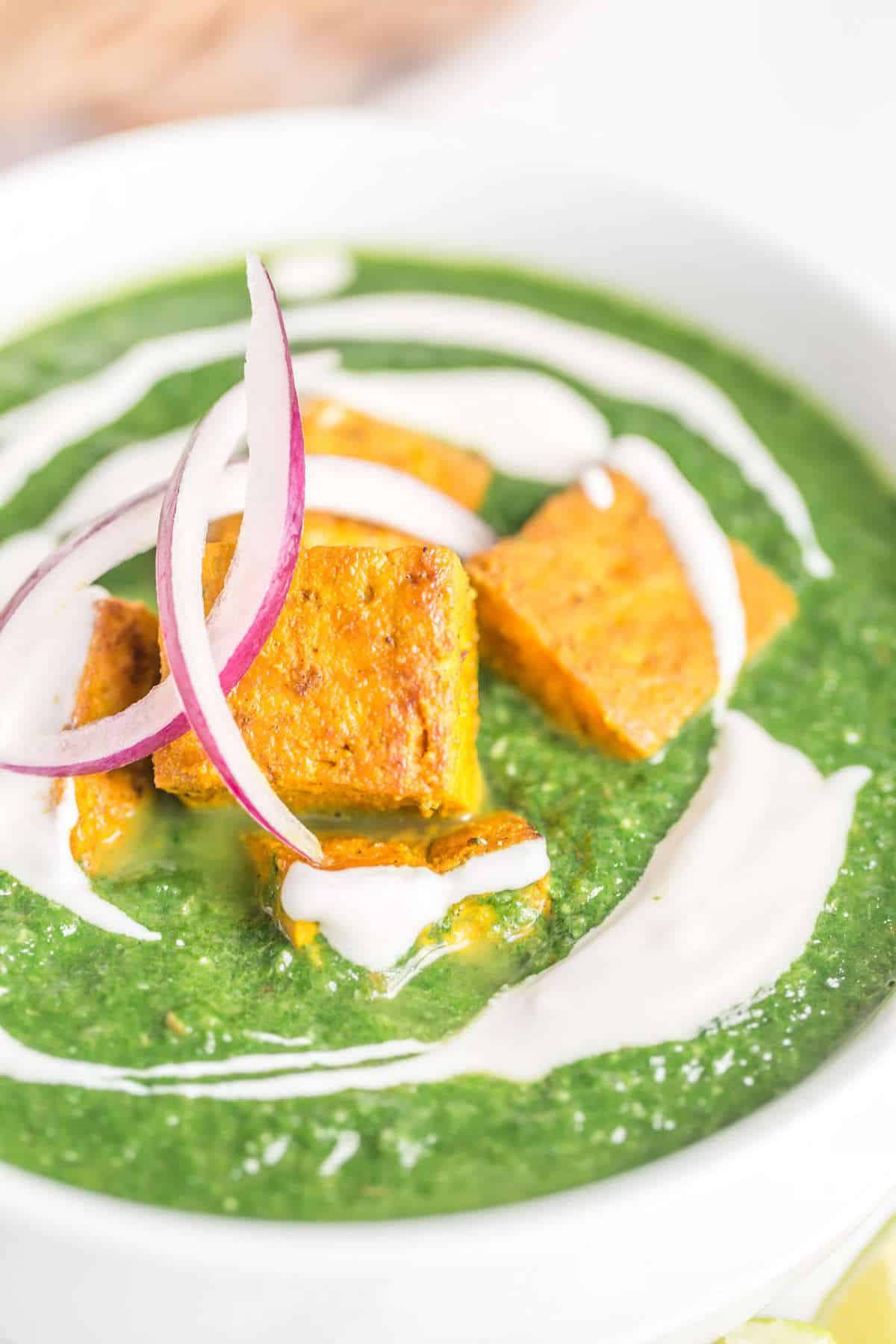 Palak tofu served in a bowl with roti and topped with red onions and vegan yogurt.