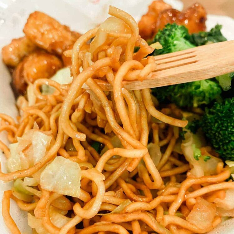 A wooden fork scooping up a bite of vegan chow mein from Panda Express.