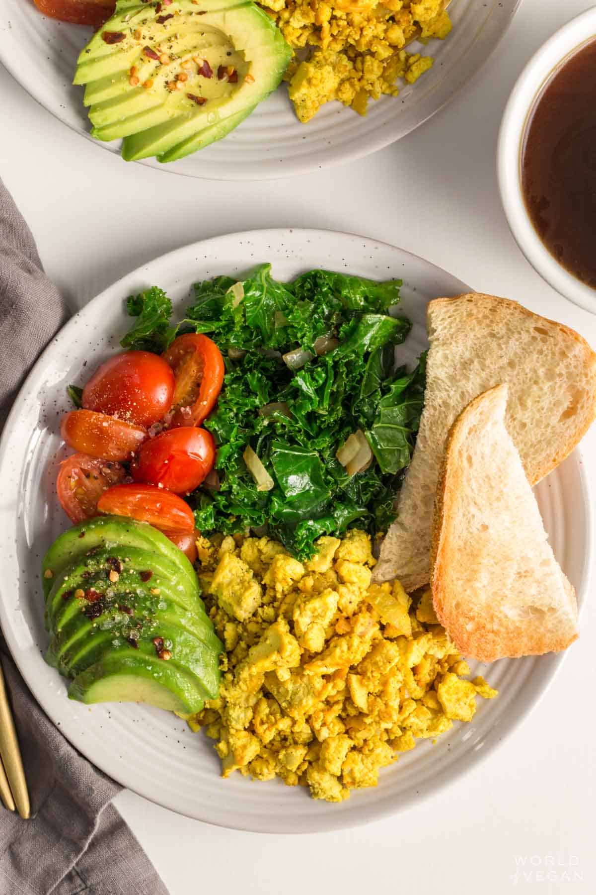 Tofu scramble served up on a vegan breakfast plate with avocado tomatoes greens and toast.