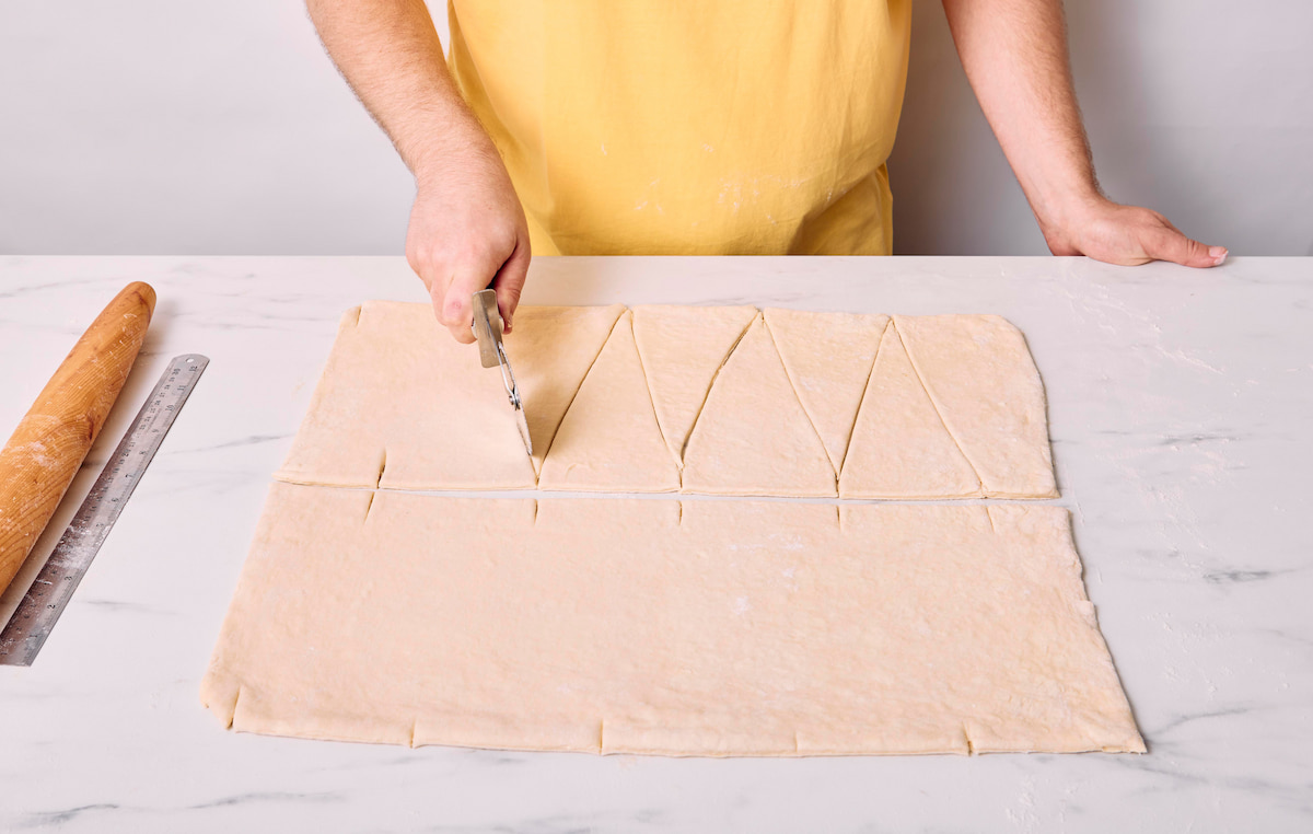 A pizza roller slicing in the the vegan croissant dough in a zigzag pattern to create triangles.