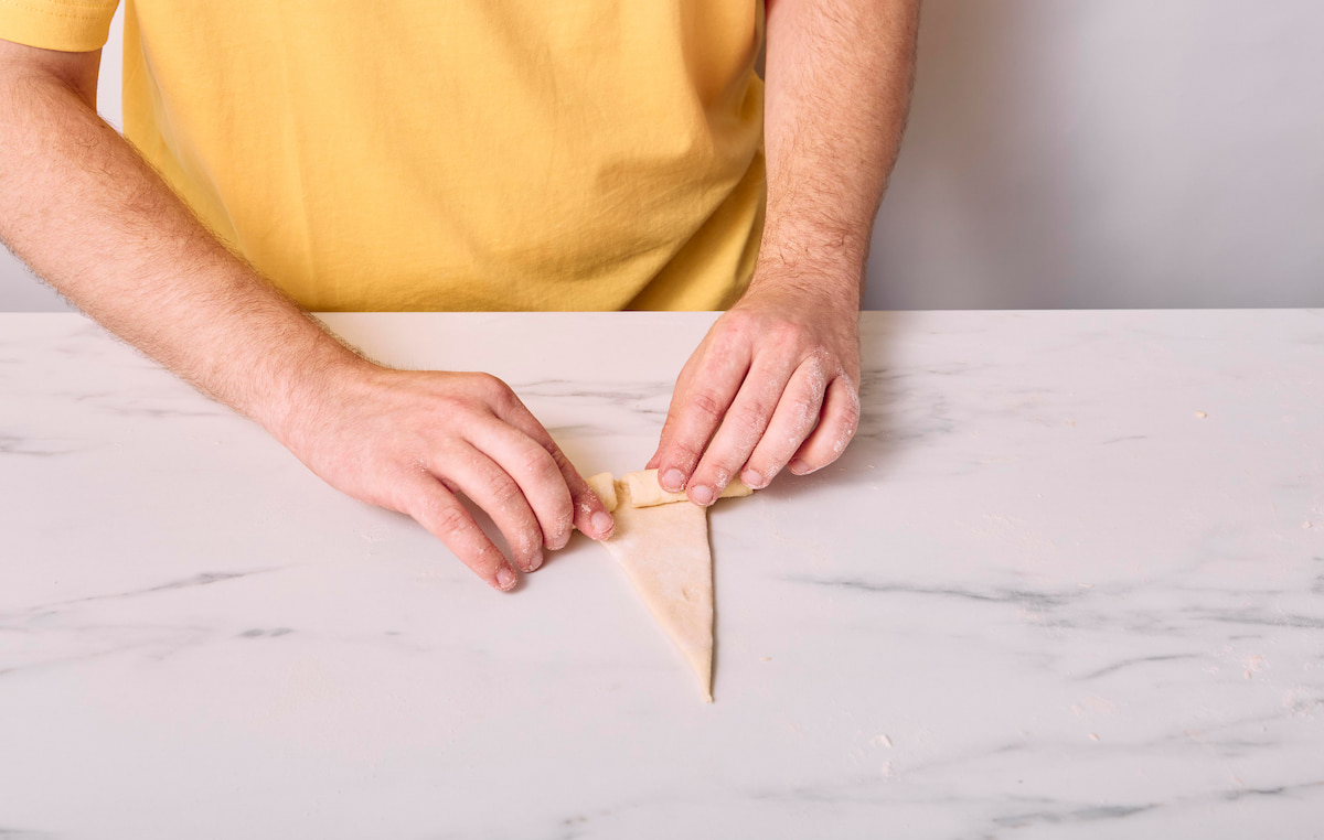 Hands rolling a vegan croissant up starting at the base of the Eiffel Tower shape.