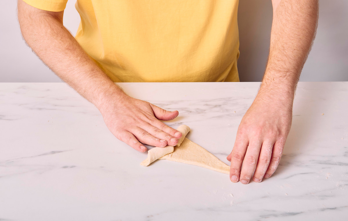 Hands rolling the vegan croissant firmly towards the top.