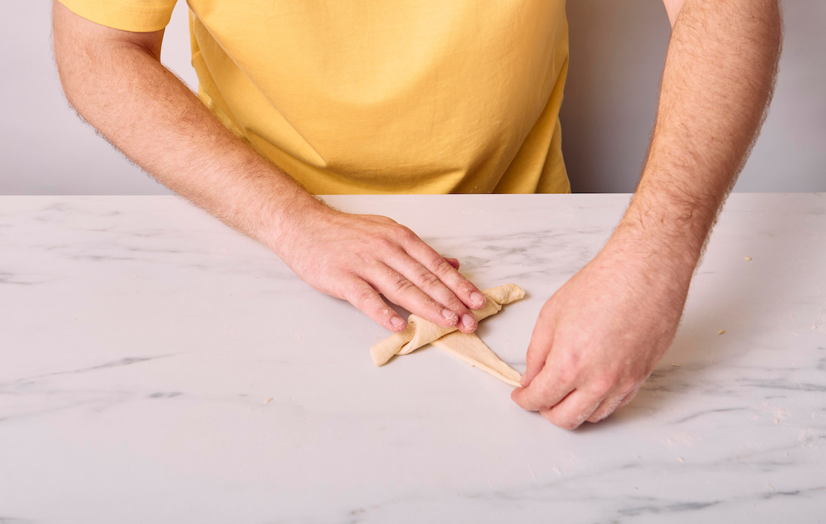Hands rolling the last part of the vegan croissant, pinching the point to firmly press it onto the croissant.