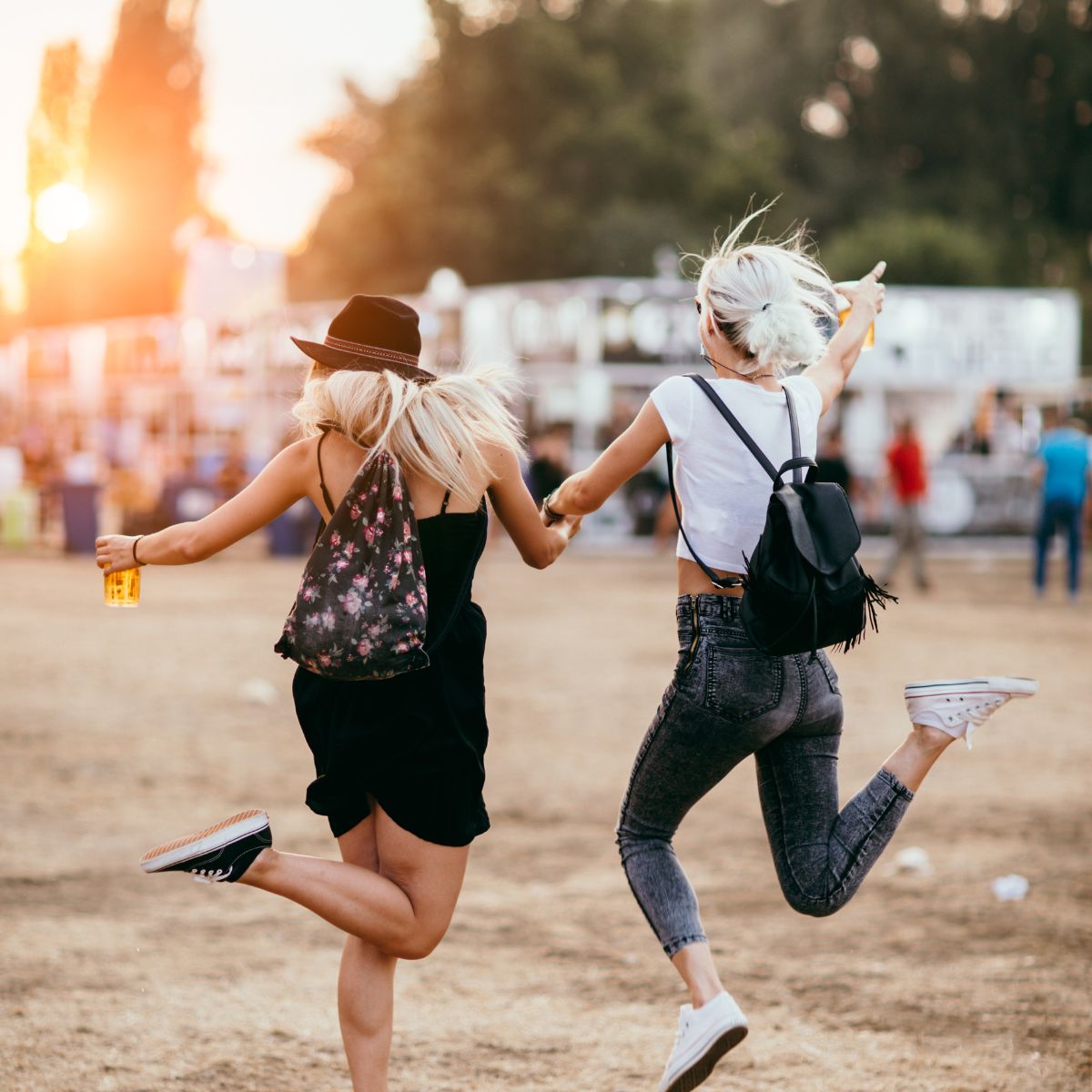 Two women holding hands and jumping at a outside festival.